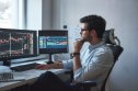 Risk reward ratio and other ways to manage risk A male trader in glasses and formal wear looking at two screens that display candle charts going up and down.