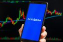 Coinbase app on a mobile phone, candlestick charts in the background