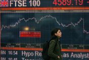 FTSE 100 board woman walking in front of FTSE 100 board