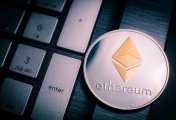 The Merge Silver Ethereum coin with gold Ethereum symbol on a laptop keyboard next to the Enter key