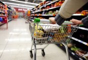 Shopper with trolley in supermarket A shopper wheels a full trolley through a supermarket aisle