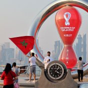 A picture taken on 20 October, 2022, shows people walking past the Qatar 2022 FIFA World Cup countdown clock as it nears marking thirty days, in the Qatari capital Doha