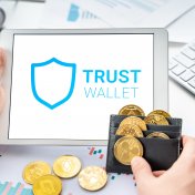 Trust Wal;l;et Token logo on screen with gold cryptocurrency coins in wallet
