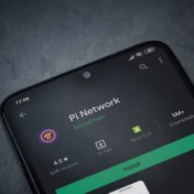 Pi Network app play store page on the display of a black mobile smartphone on dark marble stone background. Top view flat lay with copy space.