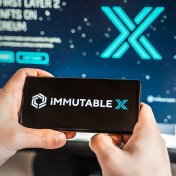 Man playing with crypto coins on a smartphone with the Immutable X logo in the background on a computer screen