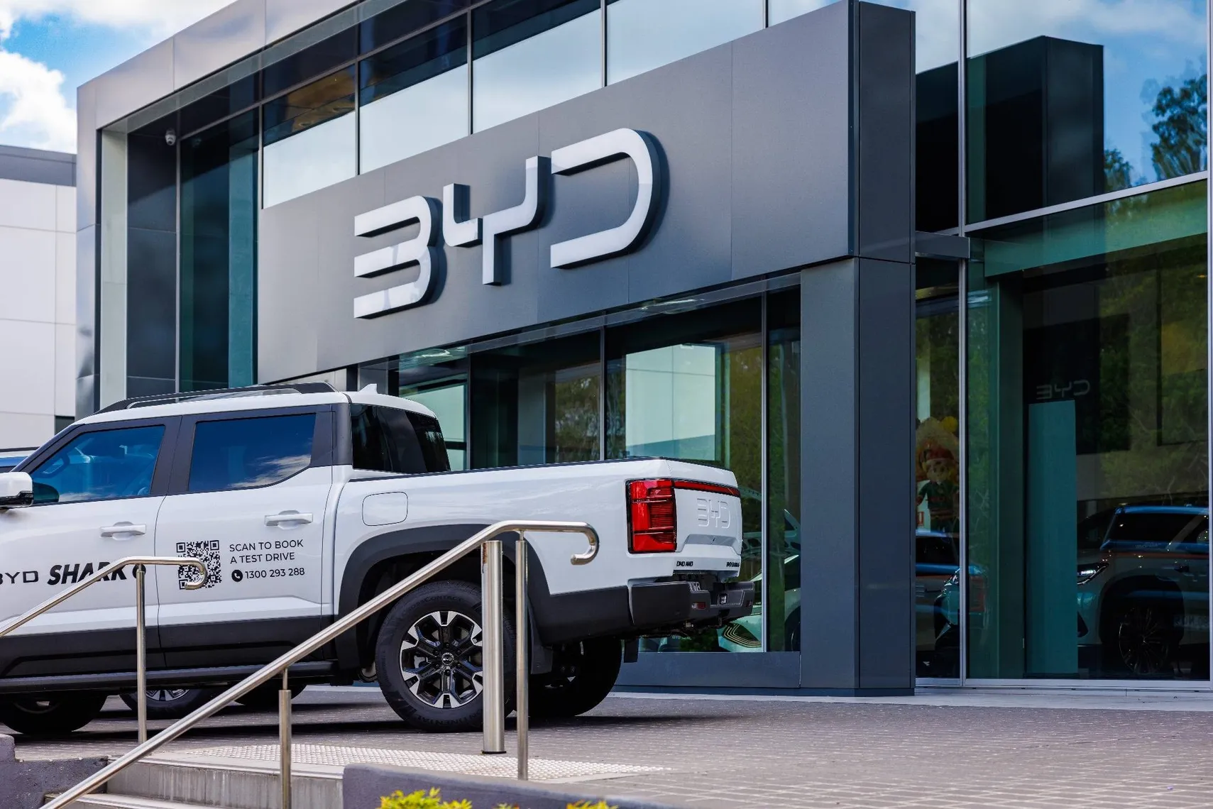 BYD showroom exterior with a white electric pickup truck parked in front of a modern glass building BYD showroom exterior with a white electric pickup truck parked in front of a modern glass building