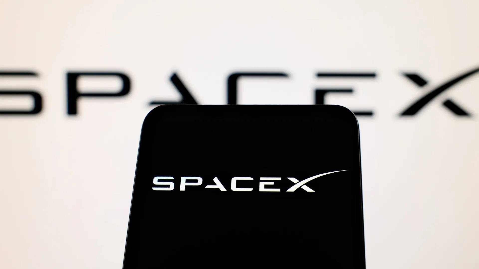 SpaceX logo displayed on a smartphone screen with a blurred SpaceX logo in the background SpaceX logo displayed on a smartphone screen with a blurred SpaceX logo in the background