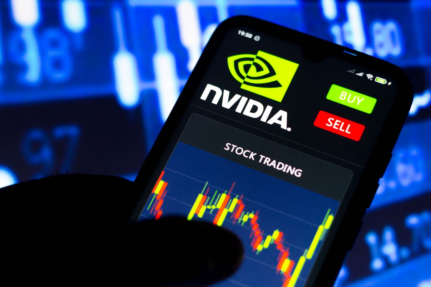 Nvidia stock split Candle charts showing Nvidia’s stock price are displayed on a mobile screen with Nvidia logo on top. There are blurred candle charts going up and down in the background.