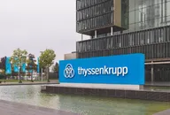 Thyssenkrupp-Logo auf einem blauen Firmenschild vor einem modernen Bürogebäude