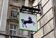 Lloyds Bank black horse logo displayed on a hanging sign outside a stone building, representing the British banking and financial services group.