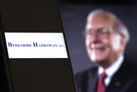 Logo di Berkshire Hathaway in primo piano con Warren Buffett sfocato sullo sfondo, simbolo della strategia prudente della holding rispetto al mercato azionario USA