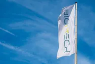 BioNTech flag on a tall pole waving against a blue sky with light clouds
