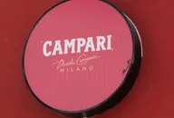 Round illuminated Campari sign mounted on a red wall with white Campari Milano branding