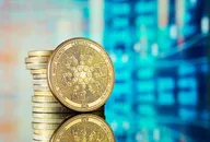 Cardano ADA Kryptowährungs-Münze steht vor gestapelten Münzen mit unscharfem digitalem Finanzmarkt-Hintergrund