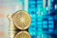 Cardano ADA cryptocurrency coin standing in front of stacked coins with a blurred digital financial market background