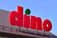 Logo supermarketu Dino umieszczone na dachu na tle czystego błękitnego nieba