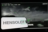 HENSOLDT-Logo auf einem mobilen Gerät mit militärtechnischen Bildern, das die Verteidigungs- und Sicherheitsbranche repräsentiert