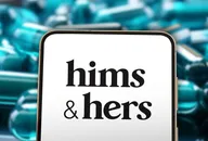 Hims & Hers logo displayed on a tablet screen with blurred capsules in the background
