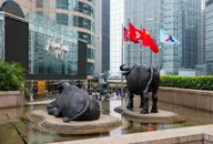 香港交易所外的牛雕塑與香港及中國國旗，背景為中環金融區辦公大樓，象徵香港股市與藍籌投資環境。