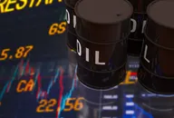Black oil barrels standing on a reflective trading screen in front of blurred stock prices and a price chart, illustrating crude oil and commodity markets
