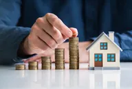Representation of increasing stacks of coins next to a model house