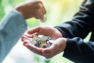 一隻手正把硬幣放入另一人捧著、裝滿零錢的雙手中。