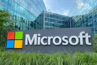 Logo Microsoft davanti a un edificio aziendale con facciata in vetro, sede del gruppo tecnologico.