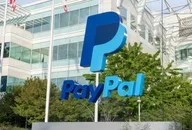 PayPal logo sign displayed outside a modern glass office building surrounded by green trees