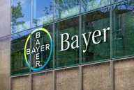 Bayer-Logo auf der Glasfassade eines modernen Bürogebäudes mit Baumreflexionen.