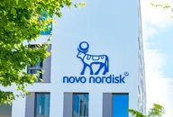 Novo Nordisk Logo an der Außenwand eines modernen Bürogebäudes mit grünen Bäumen im Vordergrund