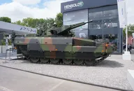 Camouflaged military armored vehicle displayed at a defense industry exhibition in front of a HENSOLDT booth