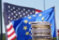 Bandiere di USA e Unione Europea con monete in primo piano, simbolo delle decisioni sui tassi di interesse di Fed e BCE
