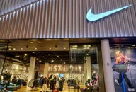 Nike-Einzelhandelsgeschäft von außen mit beleuchtetem Nike-Logo über dem Eingang und Sportbekleidung im Inneren.