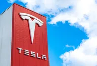 Tesla-Logo an einer roten Gebäudefassade vor strahlend blauem Himmel