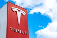 Tesla logo on a red building facade against a bright blue sky