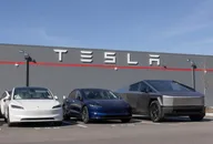 Véhicules Tesla stationnés devant un bâtiment de l'entreprise avec le logo de la société affiché sur le mur sous un ciel bleu dégagé