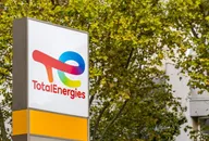 TotalEnergies logo displayed on a sign outdoors with trees and buildings in the background