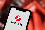 Close-up of a smartphone displaying the UniCredit logo against a blurred red background.