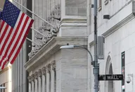 Wall Street sign beside the marble facade of the New York Stock Exchange building, with American flags flying from the exterior