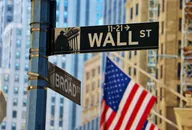 Wall Street sign with American flag and city buildings in the background