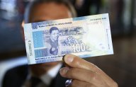 A man holds a new South African banknote at the value of one hundred South African Rand