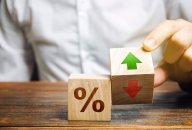 A businessman holds wooden blocks with percentages and up or down arrows. Mortgage and loan rates. Interest rate, shares, rating. The concept of business and finance.