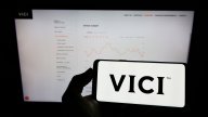 Person holding cellphone with logo of US real estate company Vici Properties Inc. on screen in front of business webpage. Focus on phone display