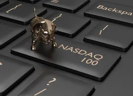 A key on a computer keyboard adapted to say NASDAQ 100, with a small gold bull charm sitting on it 