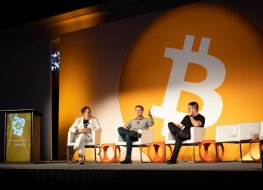 three people on stage with Bitcoin logo in the background