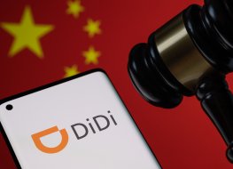 The company logo of Didi on a mobile phone next to a gavel and Chinese flag