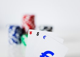 Cards at a poker table with yen, dollar and euro signs