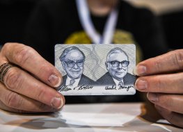 Woman shows a card with photos of Warren Buffett (L) and Charlie Munger (R) 