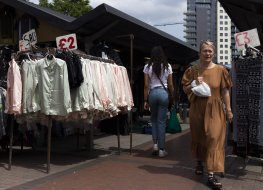 Two shoppers pass by a rack of clothes at a market