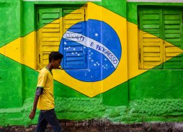 A boy wearing a Brazilian jersey is seen walking past a wall painted with the Brazilian flag